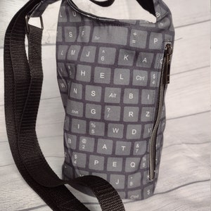 May include: A black crossbody bag with a zipper closure and a keyboard print. The bag has a long adjustable strap.