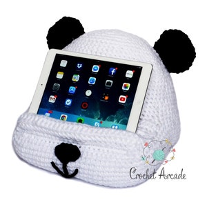Peut inclure: Support de tablette en forme de panda en crochet blanc avec des oreilles noires et un nez noir. Le support tient une tablette avec un écran lumineux affichant diverses icônes d'applications.