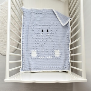 Può includere: Una coperta per neonati all'uncinetto blu chiaro con un motivo a elefante. La coperta ha bordi, piedi e orecchie bianche. Gli occhi dell'elefante sono neri. La coperta è in una culla bianca.