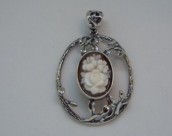 May include: A silver pendant with a cameo featuring a white rose and other flowers in a delicate floral design.
