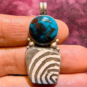 May include: A set of three ceramic mugs with a speckled, cream-colored glaze. Each mug features a different hand-painted design: a blue and green leaf, a yellow flower, and a red berry. The mugs have a simple, rounded shape.