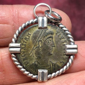 May include: A silver pendant featuring an ancient Roman coin with a profile of a person's head. The coin is surrounded by a twisted silver rope design and secured with four silver bars.