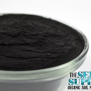 May include: A close-up of a glass bowl filled with a black powder. The bowl is sitting on a white surface. The text "THE SEED SUPPLY ORGANIC SOIL NUTRITION" is printed on the bottom of the bowl.