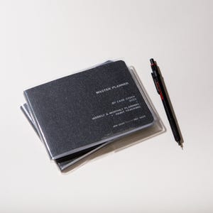 Peut inclure: Un agenda Master Planner noir avec une couverture en plastique transparent et un stylo noir avec des d&eacute;tails rouges. L'agenda contient le texte "Master Planner", "By Case Study 2025" et "Weekly & Monthly Planning + Habit Tracking". Les dates sont de janvier 2025 &agrave; d&eacute;cembre 2025.