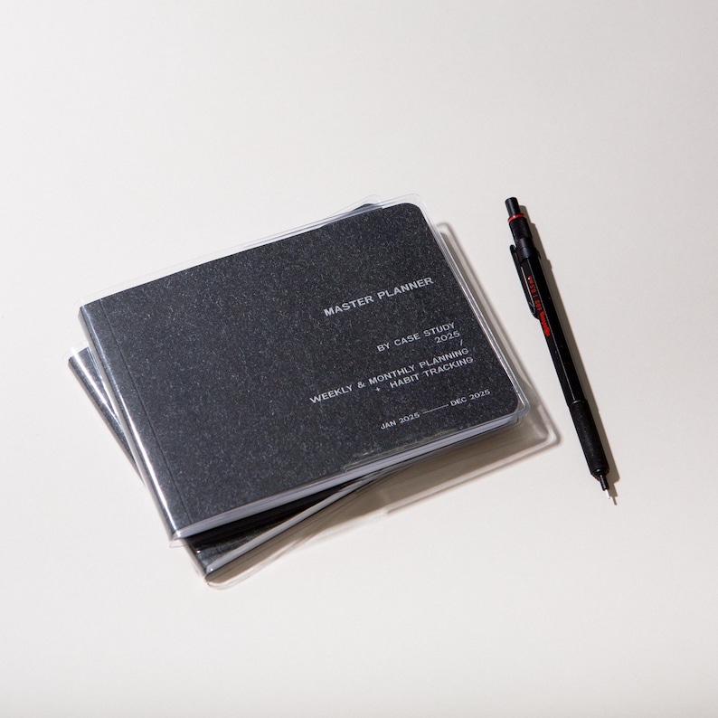 Peut inclure: Un agenda Master Planner noir avec une couverture en plastique transparent et un stylo noir avec des d&eacute;tails rouges. L'agenda contient le texte "Master Planner", "By Case Study 2025" et "Weekly & Monthly Planning + Habit Tracking". Les dates sont de janvier 2025 &agrave; d&eacute;cembre 2025.