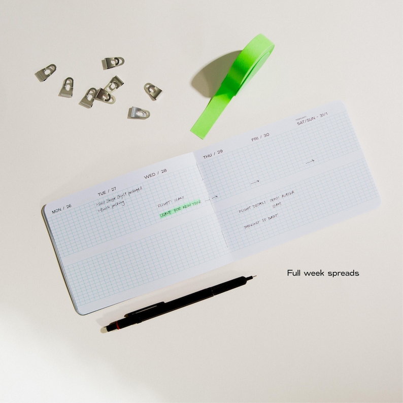 Peut inclure: Un carnet ouvert avec du papier quadrill&eacute;, un stylo noir et un post-it vert. Le carnet est ouvert sur une semaine, avec des notes manuscrites. De petits clips argent&eacute;s sont &eacute;parpill&eacute;s autour du carnet. Le texte sur la page indique "Full week spreads."