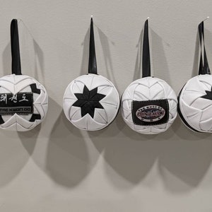 May include: Four white and black fabric ornaments with different designs hanging from black strings. The ornaments have a star, a Tae Kwon Do logo, and a Tae Kwon Do logo with the words "The Kwon Do of Punching" in a circle.