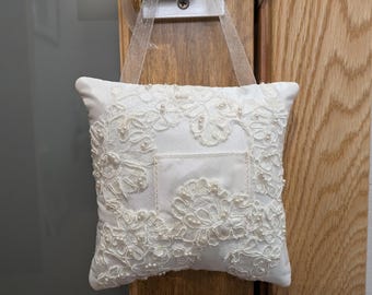 May include: White lace pillow with a pocket in the center, hanging from a door with a white ribbon.