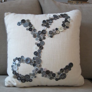 May include: A white pillow with a design of black and gray buttons arranged in the shape of an infinity symbol.