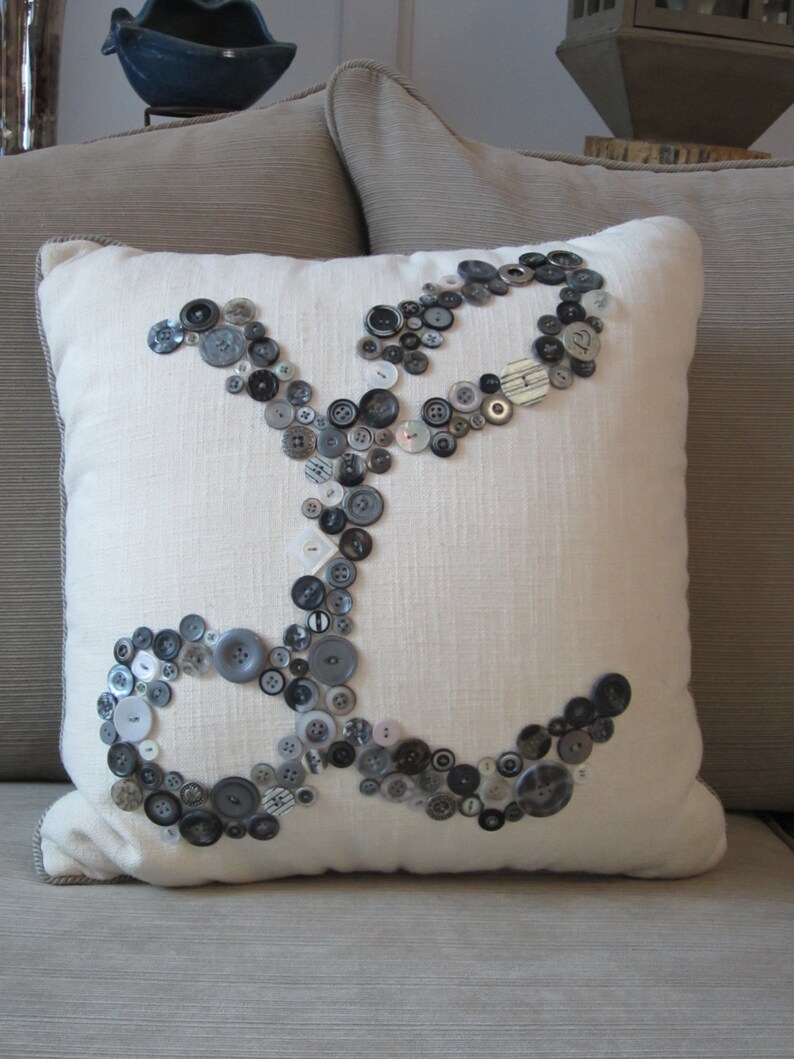May include: A white pillow with a design of black and gray buttons arranged in the shape of an infinity symbol.