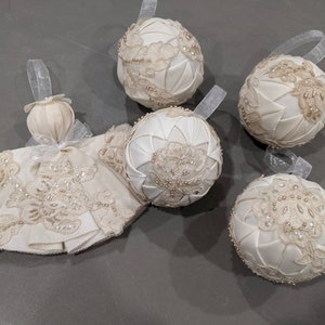 May include: Five white satin Christmas ornaments with lace and pearl embellishments. The ornaments are round and have a quilted design.