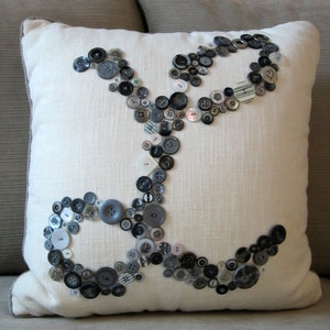May include: A white pillow with a design of black and white buttons arranged in a pattern. The buttons are of various sizes and shapes.