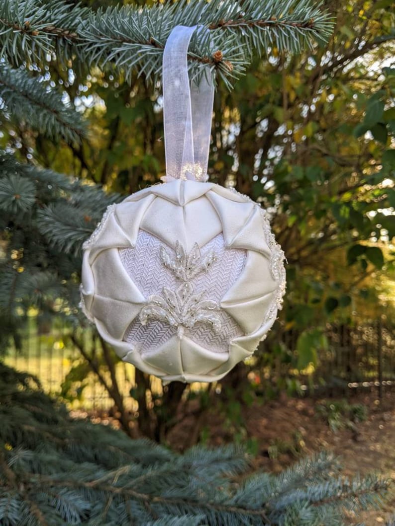 May include: A white fabric Christmas ornament with a beaded design and a white satin ribbon.