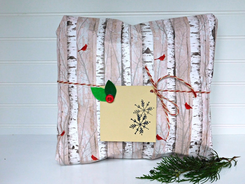 May include: A gift wrapped in birch tree patterned paper with red robins and a snowflake gift tag. The gift is tied with twine and decorated with green leaves.