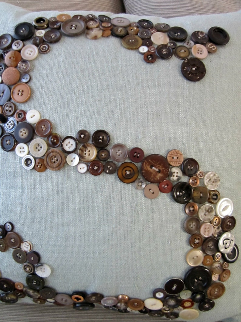 May include: A light blue pillow with a decorative design of brown, black, and white buttons arranged in a swirling pattern.