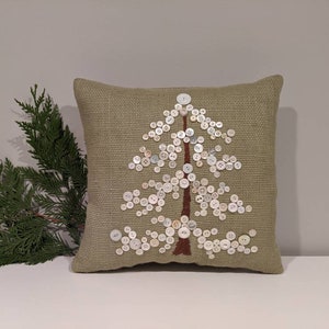 May include: A green throw pillow with a white button tree design. The pillow is made of a textured fabric and has a brown stem.