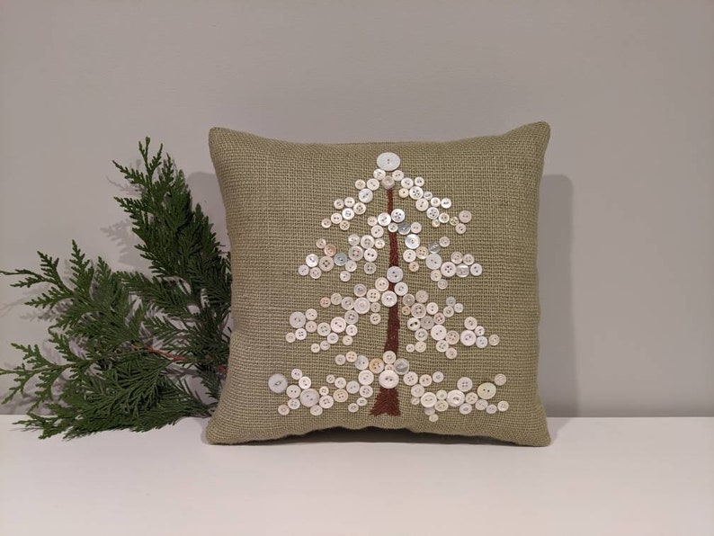 May include: A green throw pillow with a white button tree design. The pillow is made of a textured fabric and has a brown stem.