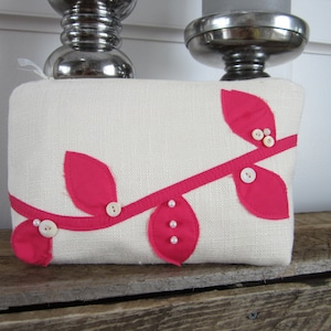 May include: A white linen cosmetic bag with a pink fabric branch design and white pearl buttons.