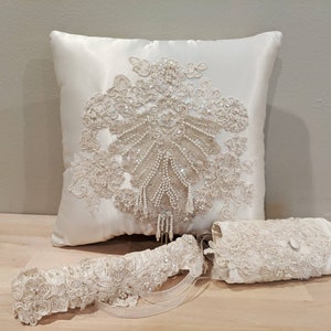 May include: A white satin pillow with a beaded and lace design, a white lace garter, and a white lace clutch.