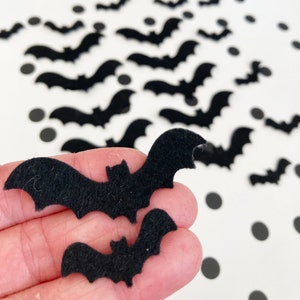 Peut inclure: Des découpes de chauves-souris en feutre noir sur un fond blanc avec des pois noirs. Les chauves-souris sont de différentes tailles et sont dispersées sur la surface. Une chauve-souris est tenue par une main.