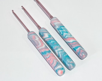 May include: Three crochet hooks with pink and blue marbled handles. The hooks are different sizes and are arranged in a row.
