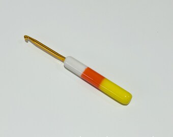 May include: A candy cane-colored crochet hook with a gold hook and a white, orange, and yellow handle.