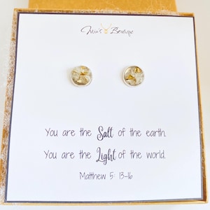 May include: A pair of silver stud earrings with a clear resin base and gold flecks. The earrings are displayed on a white card with the text "You are the Salt of the earth. You are the Light of the world. Matthew 5: 13-16".