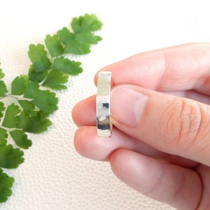 Puede incluir: Un anillo de banda martillado de plata. El anillo es simple y elegante, con un acabado liso y pulido.