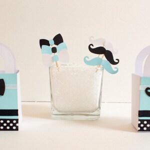 May include: Three light blue favor boxes with white polka dots and black trim. Each box has a different black and white paper cutout on the front: a bow tie, a mustache, and a bow tie with a mustache.