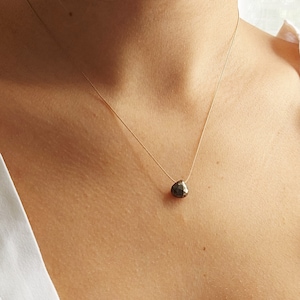 Puede incluir: Un delicado collar de cadena dorada con un solo colgante de piedra preciosa gris oscuro facetado.