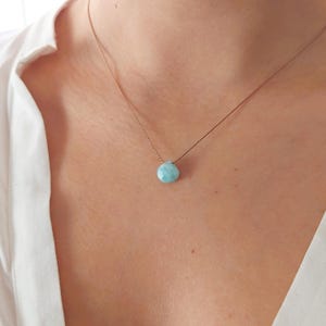 以下が含まれることがあります： 薄い茶色の紐に、薄い水色の宝石のペンダントがついた、繊細なネックレス。ペンダントは涙の形をしています。