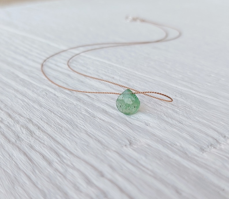 May include: A delicate green gemstone pendant necklace on a brown cord.