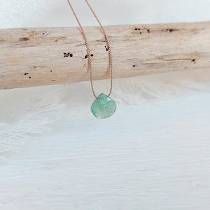 May include: A green gemstone pendant necklace on a brown cord. The pendant is a teardrop shape and has a faceted finish.