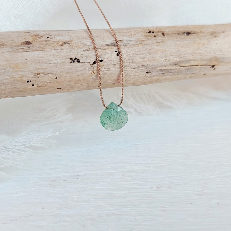 May include: A green gemstone pendant necklace on a brown cord. The pendant is a teardrop shape and has a faceted finish.