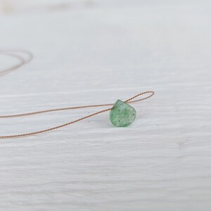 May include: A green gemstone pendant on a brown cord necklace. The pendant is a teardrop shape and has a rough, natural texture.