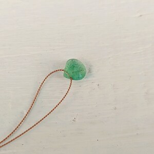 May include: A green gemstone bead with a brown cord threaded through it.