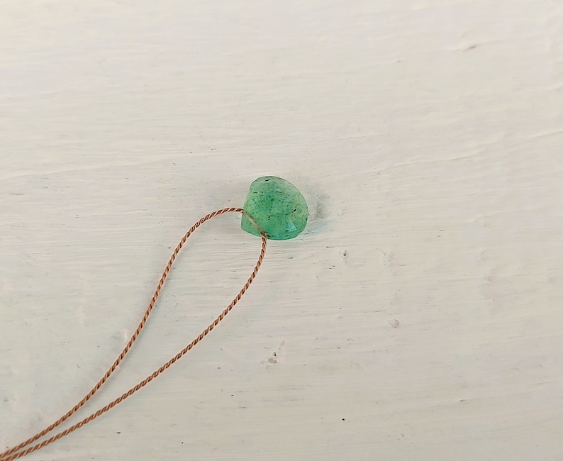 May include: A green gemstone bead with a brown cord threaded through it.