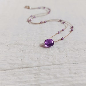 Puede incluir: Un collar delicado con un colgante de amatista púrpura grande y único. El collar está hecho de una cadena fina de color dorado con pequeñas cuentas púrpuras.