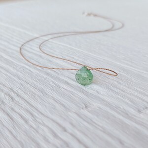 May include: A delicate green gemstone pendant necklace on a brown cord.
