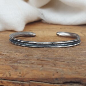Peut inclure: Un bracelet en argent avec une finition texturée et martelée. Le bracelet a un design simple et minimaliste et est fait d'une seule bande de métal.