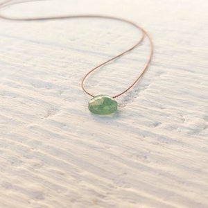 May include: A delicate green gemstone necklace with a simple brown cord.