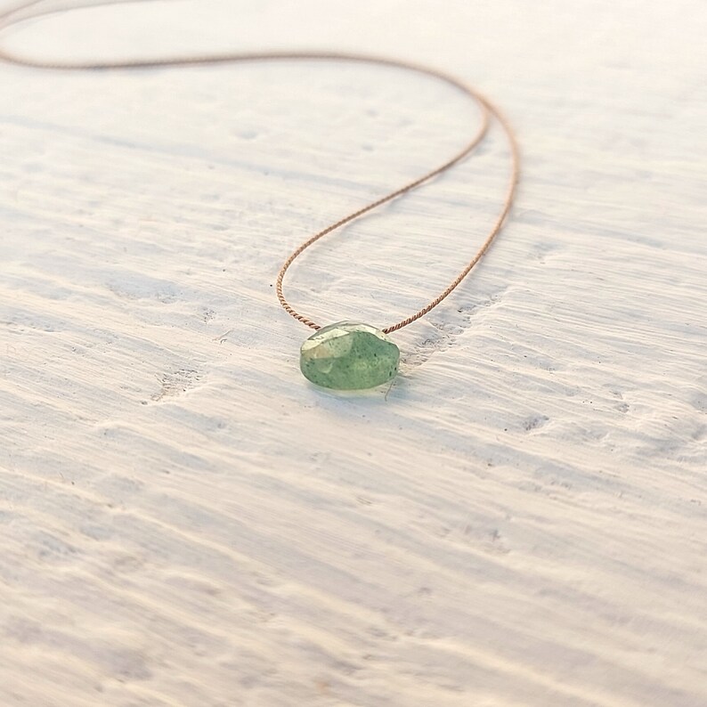 May include: A delicate green gemstone necklace with a simple brown cord.