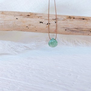 May include: A green gemstone pendant on a brown cord necklace. The pendant is a teardrop shape and has a speckled appearance.