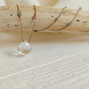 Könnte beinhalten: Eine zarte Halskette mit einem großen, klaren Quarzkristall-Anhänger. Die Halskette ist aus braunem Band gefertigt und hat kleine, bunte Perlen.