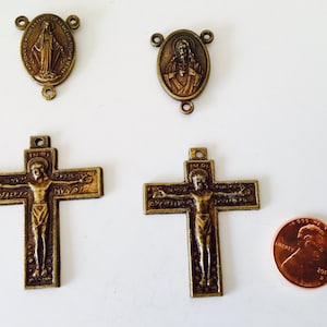 Puede incluir: Colgantes y cruces religiosos antiguos de bronce. La imagen muestra dos colgantes ovalados, dos cruces con la figura de Jesús y una moneda de un centavo. Los colgantes representan figuras religiosas. Las cruces tienen la inscripción INRI.