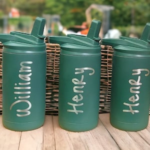 Puede incluir: Tres botellas de agua de acero inoxidable verdes con tapas abatibles y pajitas. Las botellas est&aacute;n personalizadas con los nombres "William", "Henry" y "Henry".