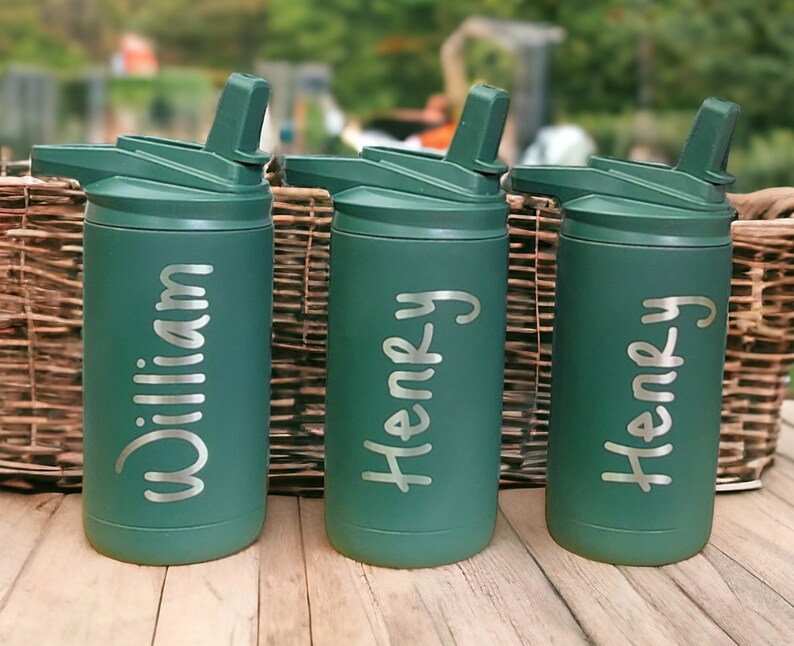 Puede incluir: Tres botellas de agua de acero inoxidable verdes con tapas abatibles y pajitas. Las botellas est&aacute;n personalizadas con los nombres "William", "Henry" y "Henry".