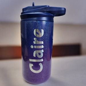 Puede incluir: Un vaso azul y morado con purpurina, con una tapa azul marino y el nombre "Claire" en plata en el lateral.