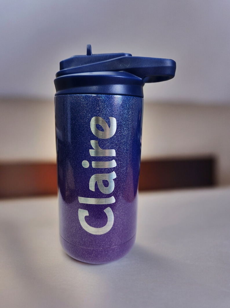 Puede incluir: Un vaso azul y morado con purpurina, con una tapa azul marino y el nombre "Claire" en plata en el lateral.