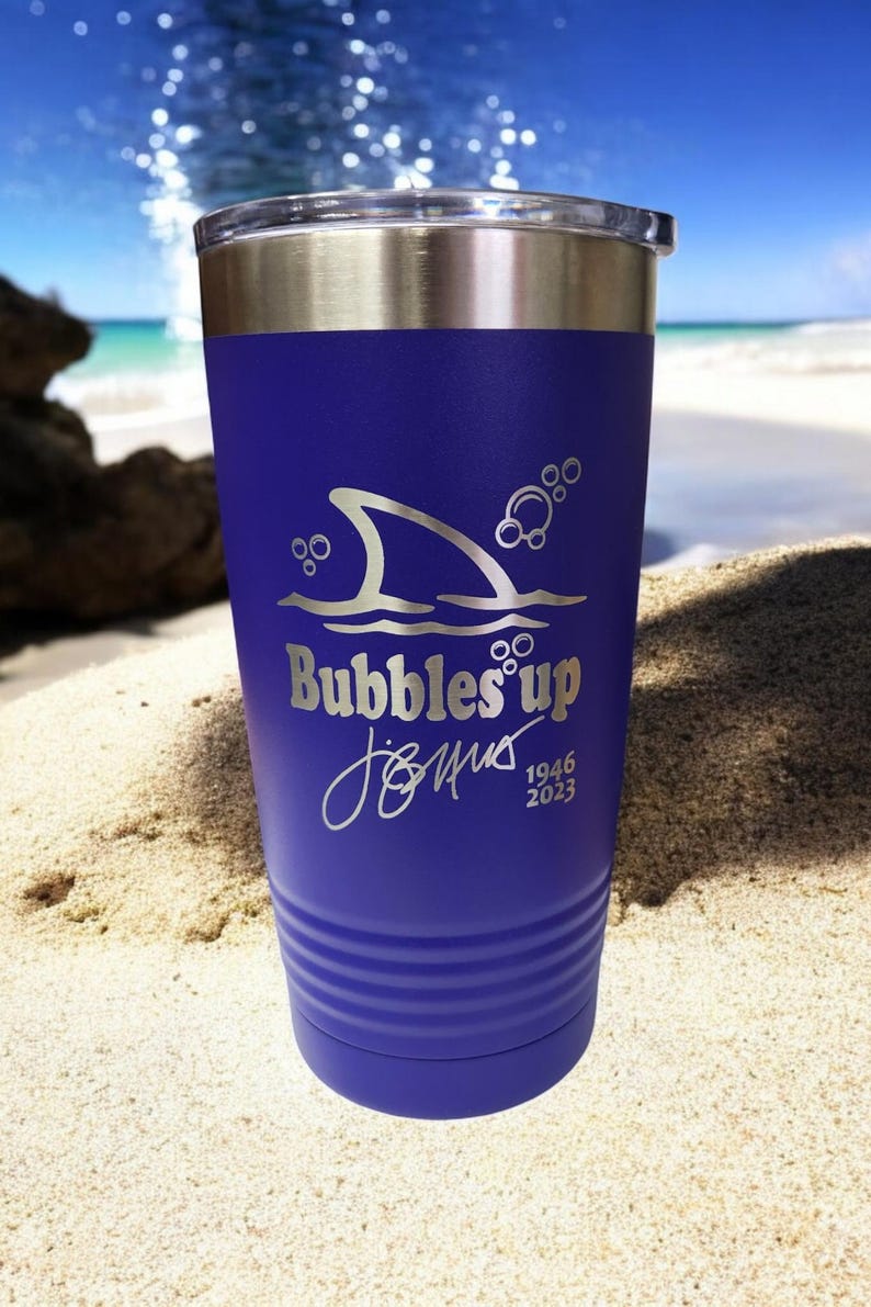 May include: A purple stainless steel tumbler with a shark fin and bubbles design. The tumbler has the text "Bubbles Up" and "Jimus 1946 2023" engraved on it.
